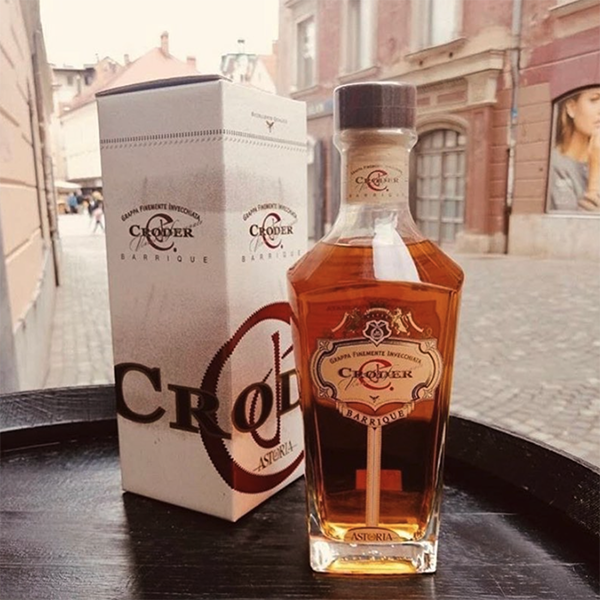 Botella de Grappa Barrique Croder de Astoria Wines con su estuche, sobre mesa en entorno urbano italiano